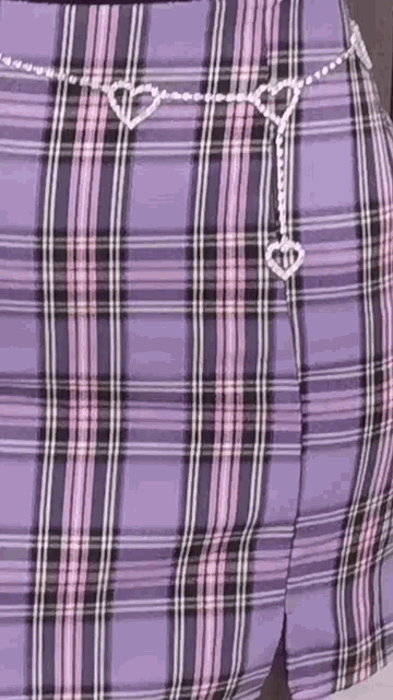 a woman is wearing a purple plaid skirt with a heart shaped chain around her waist .