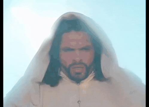 a man with long hair and a beard is wearing a white robe with a hood on his head .