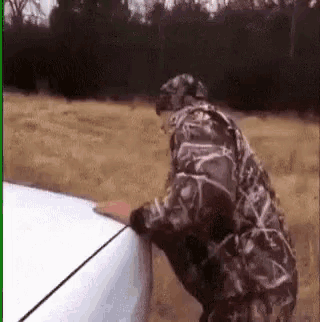 a man in a camouflage jacket is standing next to a white truck .