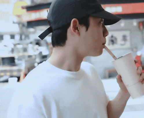 a man wearing a black hat is drinking through a straw from a cup