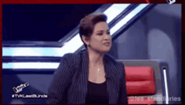 a woman in a striped jacket is sitting on a red chair on a tv show