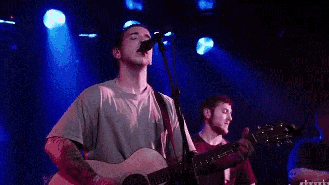 a man is singing into a microphone while another man plays a guitar on a stage .