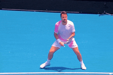 a man in a white shirt and pink shorts is holding a tennis racquet on a blue court