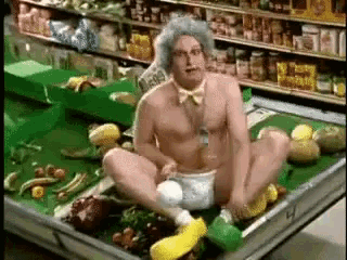 a naked man in a diaper is sitting on a tray of fruit and vegetables in a grocery store .