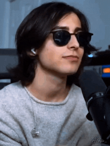 a young man with long hair is wearing sunglasses and headphones while talking into a microphone .