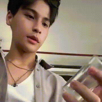 a young man wearing sunglasses and a white shirt is holding a glass in his hand .