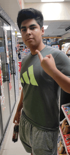 a young man wearing a grey adidas shirt is pointing to his chest
