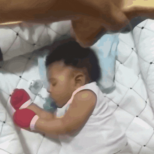 a baby wearing boxing gloves sleeps on a bed