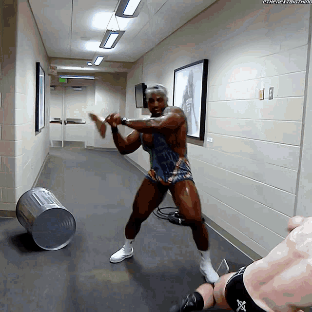 a man in a wrestling outfit is standing in a hallway with a trash can in the background