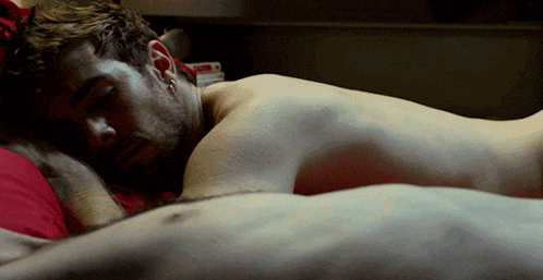 a man laying on another man 's stomach with a red pillow