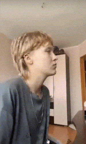 a person with blonde hair is wearing a blue shirt and a chain around their neck