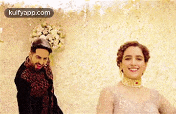 a man and a woman are standing next to each other and smiling . the woman is wearing a wedding dress .