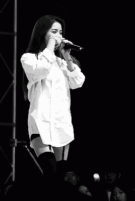 a black and white photo of a woman singing into a microphone on stage .