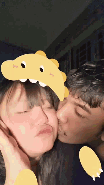 a man kissing a girl wearing a yellow dinosaur hat