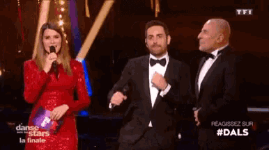 a woman in a red dress is speaking into a microphone next to two men in suits