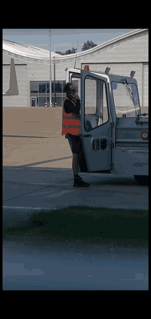 a man in an orange vest is talking on a cell phone while standing next to a white vehicle