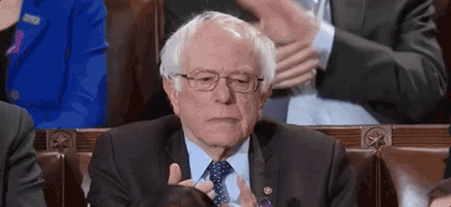 a man in a suit and tie is sitting in a row of chairs and clapping .