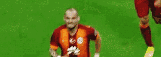 a soccer player in a red and orange jersey is walking on a green field .