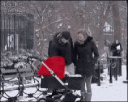 a man and woman are standing next to a red stroller in the snow .