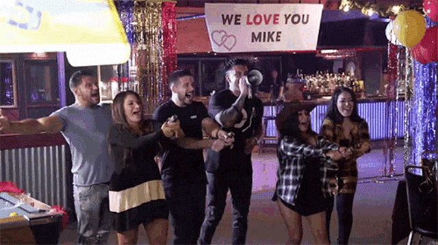 a group of people are standing around a sign that says we love you mike .