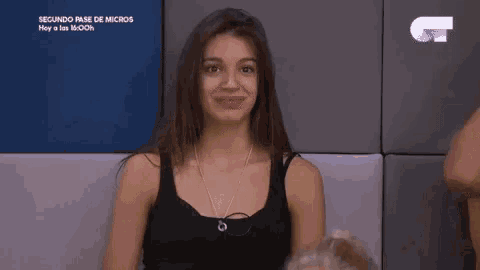 a woman in a black tank top is sitting in front of a blue wall .