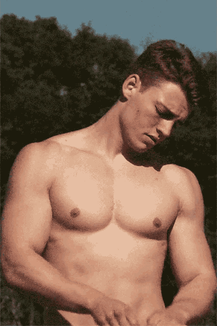 a man without a shirt is standing in front of trees