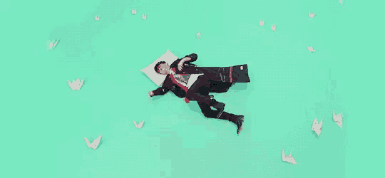 a man is laying on the floor with a pillow and a suitcase surrounded by paper butterflies .