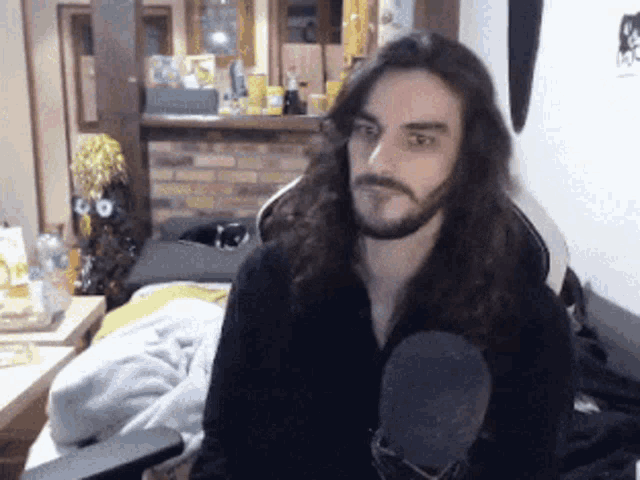 a man with long hair and a beard is sitting in front of a microphone in a living room