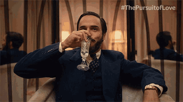 a man in a suit is drinking from a glass with the #thepursuitoflove written on the bottom
