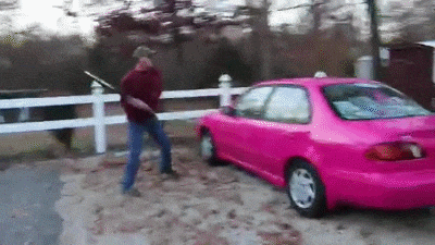 a man is standing next to a pink car in a parking lot .