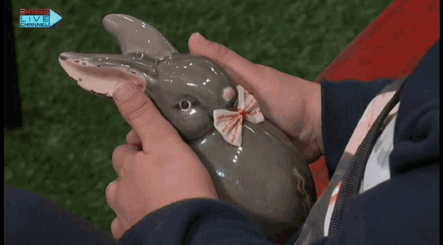 a person is holding a ceramic rabbit with a bow in front of a 24hrs live channel logo