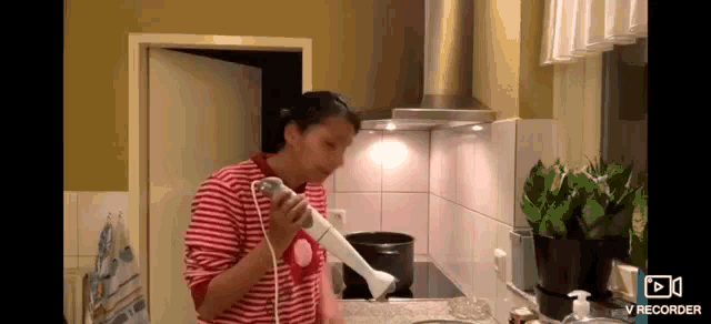 a woman in a red and white striped shirt is holding a hand blender in a kitchen .