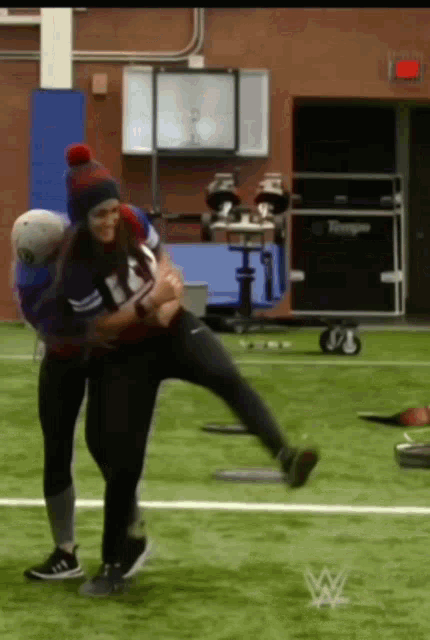 a man is carrying a woman on his back on a field with a wwe logo in the background
