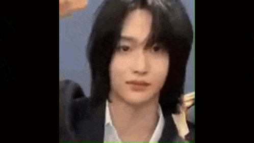 a close up of a young man with long black hair wearing a suit and a white shirt .