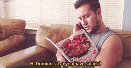 a man is sitting on a couch talking on a cell phone while reading a pan pizza magazine