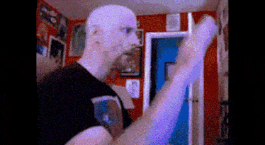 a bald man with a beard is standing in front of a red wall
