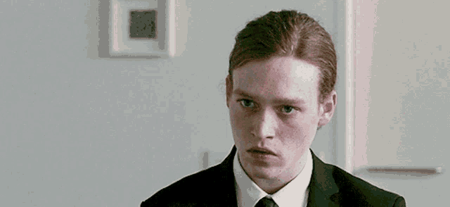 a man with red hair is wearing a suit and tie and looking at the camera .