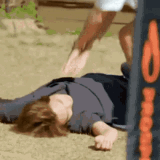 a person is laying on the ground with their feet up and another person is jumping over them .