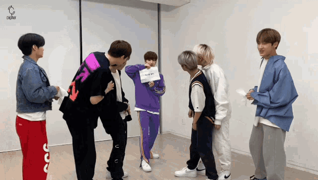 a group of young men are standing in a room and one of them has a sign on his back that says ' x '
