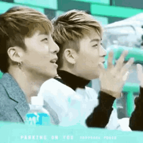 two young men are sitting next to each other in a stadium with their hands in the air .