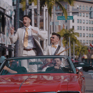 two men in suits and bow ties are riding in a red convertible .