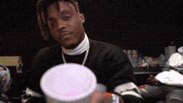 a man in a black sweater and white turtleneck is holding a white cup .