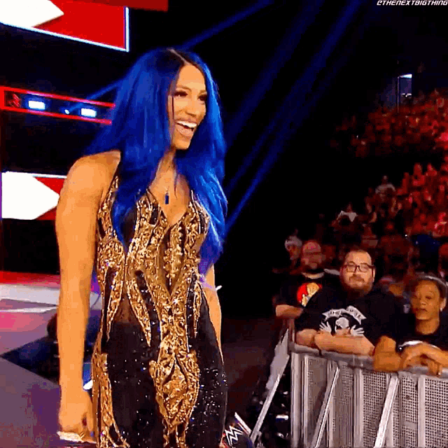 a woman with blue hair is standing in front of a crowd in a wrestling ring .