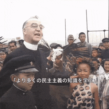 a man in a white collared shirt stands in front of a crowd with chinese writing on the bottom right