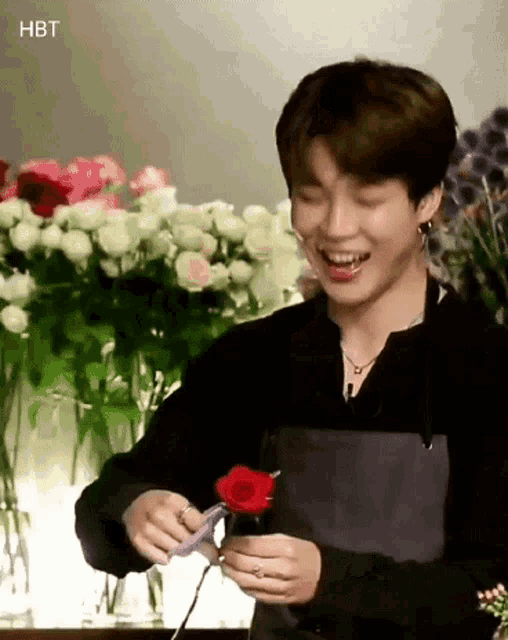 a man in an apron is holding a red rose and smiling in front of a bunch of flowers .