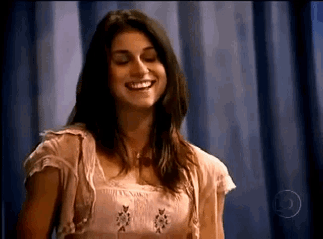 a woman in a pink top is smiling in front of a blue curtain with the number 5 on it