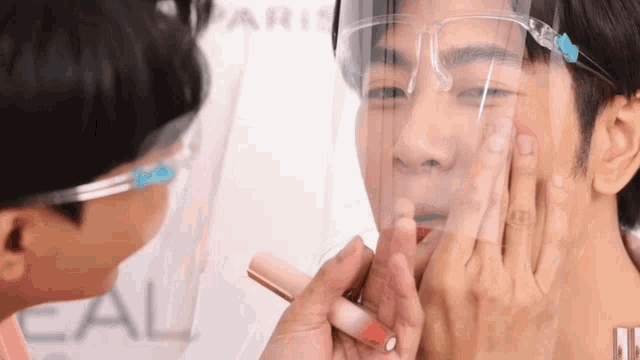 a man wearing a face shield is getting his lips painted .
