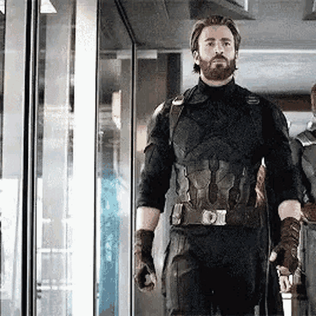 a man with a beard is standing in front of a glass door in a room .