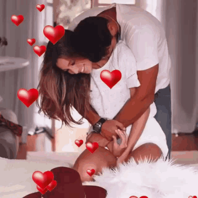 a man is hugging a woman on a bed surrounded by red hearts .