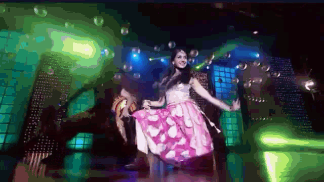 a woman in a pink dress is dancing on a stage with bubbles